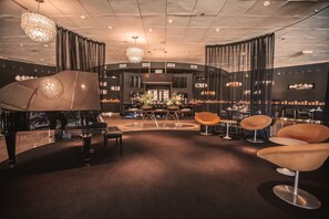 Ein Flügel, moderne Stühle, eine Bar und eine Kristallleuchter in einer geräumigen Lobby.