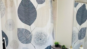 A bathroom with a shower curtain featuring leaf patterns, a toilet, a sink with a mirror, and a small potted plant on the counter.
