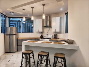 Una cocina moderna con un refrigerador de acero inoxidable, una estufa a gas y tres taburetes de bar.
