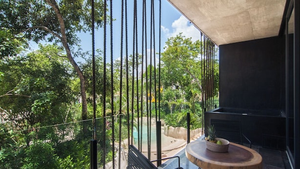 Ein Balkon mit rundem Tisch und Stühlen, mit Blick auf einen Swimmingpool und üppige Bepflanzung.