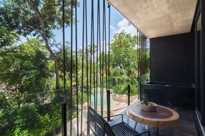 Uma varanda com uma mesa redonda e cadeiras, com vista para uma piscina e vegetação exuberante.