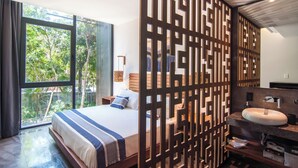 Ein modernes Schlafzimmer mit einem großen Bett, ein Badezimmer mit Waschbecken und Spiegel sowie Blick auf Grünfläche.