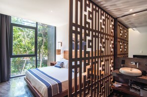 Quarto moderno com cama grande, banheiro com pia e espelho, e vista para o verde lá fora.