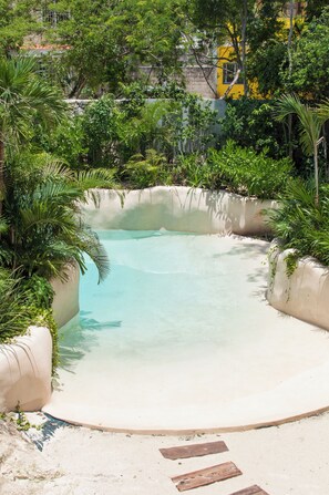 Uma piscina límpida cercada por vegetação exuberante e um edifício amarelo ao fundo.
