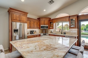 A kitchen with wooden cabinets, stainless steel appliances, a marble island, and a view of the outdoors. - Waterfront 3BR Home with Pool ,BBQ Patio & Fire Pit (Glendale)