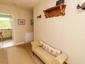 A living room with a sofa, a wooden shelf, a radiator, and a window leading to a kitchen. - Campden (Alnwick)