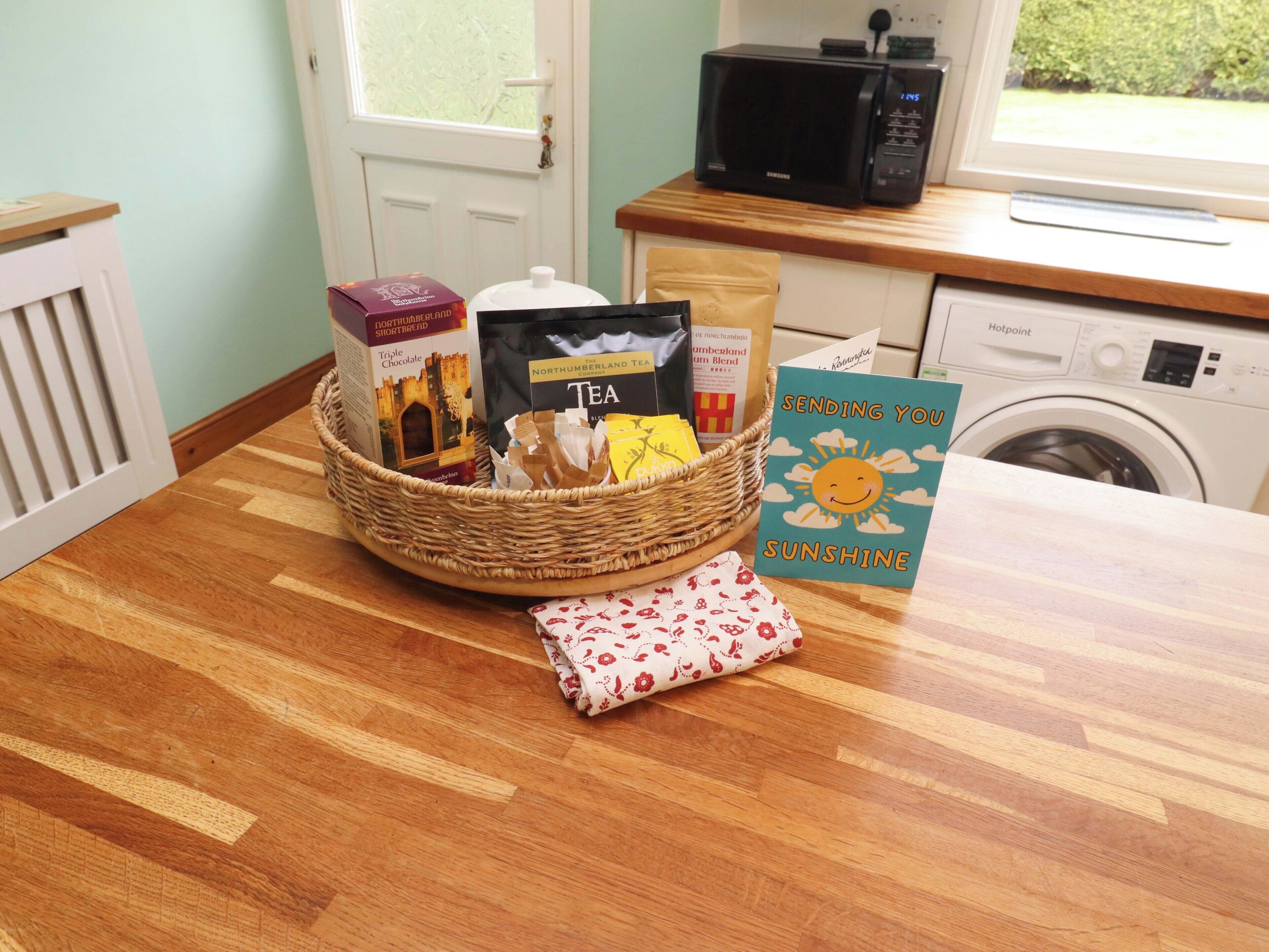 A kitchen with a microwave, a basket of groceries, and a card on the counter.