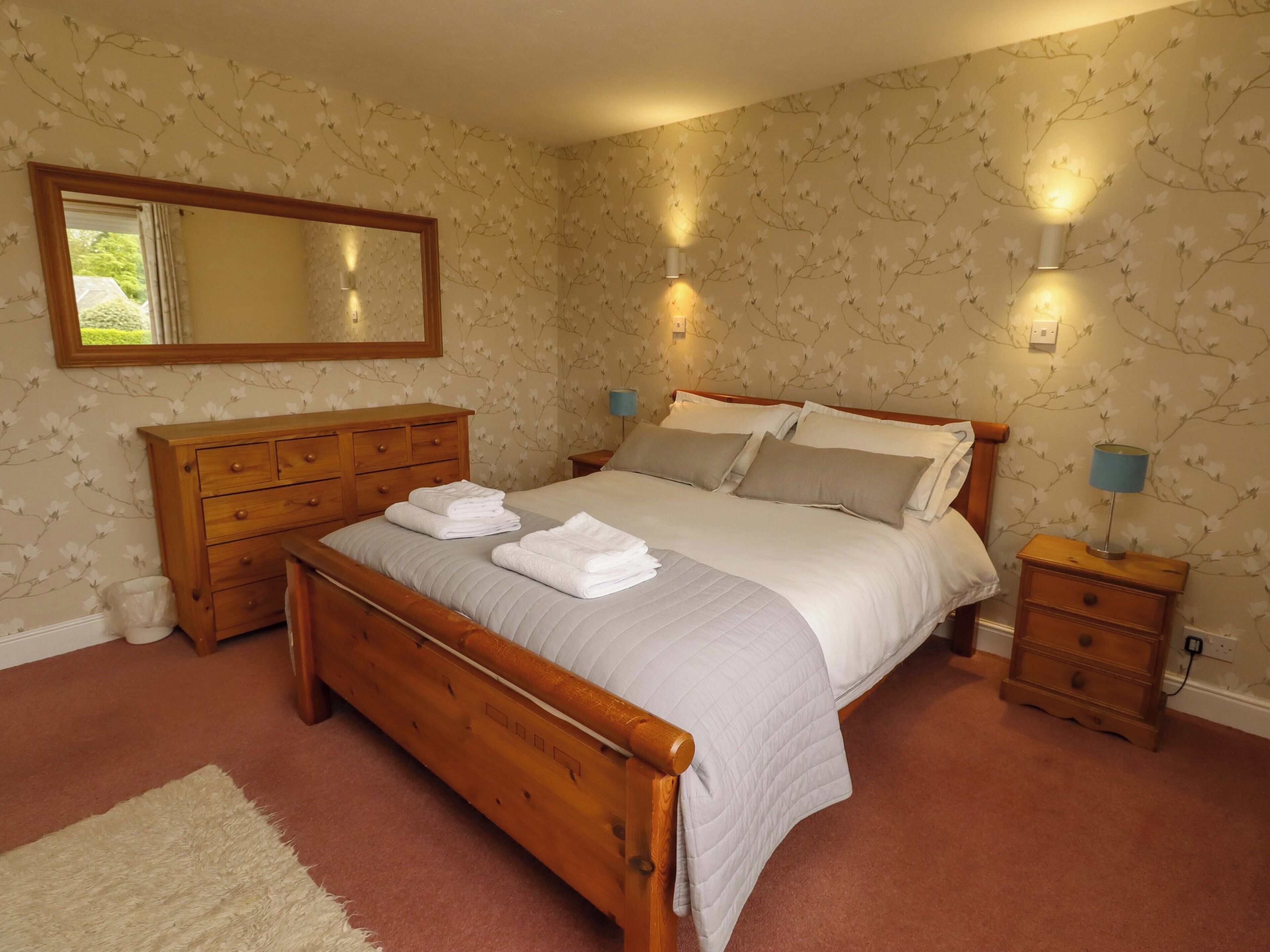 A bedroom with a wooden bed, a dresser, a mirror, and two bedside lamps.