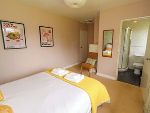 A hotel room with a bed, a chair, a bathroom with a toilet and shower, and two framed pictures on the wall. - Campden (Alnwick)