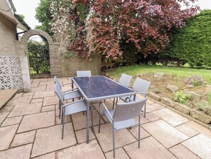 A patio with a square table and six chairs, surrounded by stone tiles. - Campden (Alnwick)