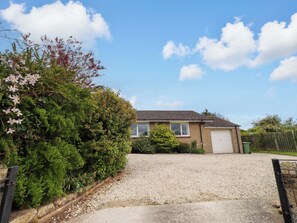 A residential house with a gravel driveway, a garage, and a garden with various plants and flowers. - Campden (Alnwick)