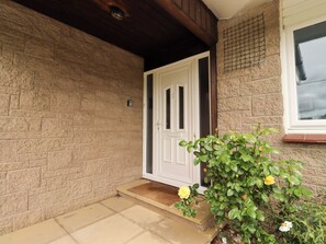 A stone wall, a white door, and a small garden with a yellow flower. - Campden (Alnwick)