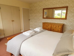 A bedroom with a bed, a wooden dresser, a mirror, and a wardrobe. - Campden (Alnwick)