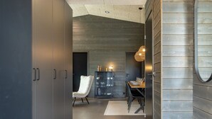A modern interior with a dark-toned wardrobe, a white chair, a dining table with chairs, and a hanging light fixture.
