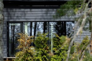 Moderni rakennus, jossa on suuret ikkunat ja joka on ympäröity tiheällä metsällä.