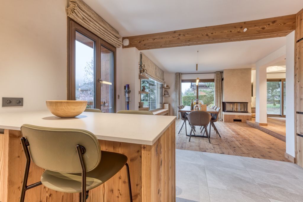 A modern kitchen with a large island, wooden beams, and a dining area with a fireplace.