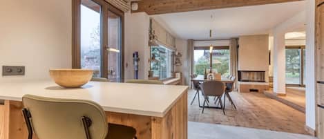 A modern kitchen with a large island, wooden beams, and a dining area with a fireplace.