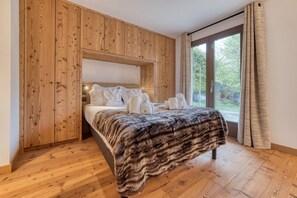 Ein Schlafzimmer mit einem hölzernen Kopfteil, einem Bett mit weißer Bettwäsche, einem Fellüberwurf und einem großen Fenster mit Vorhängen.
