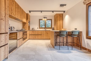 Eine moderne Küche mit Holzschränken, einer zentralen Kochinsel, Barhocker und einem Fenster für natürliches Licht.
