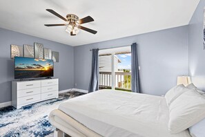 Un dormitorio con cama, ventilador de techo, televisión y vista al exterior.