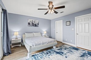 Ein Schlafzimmer mit einem Bett, Nachttischlampen, einem Deckenventilator, einer Tür und einer Wand mit einem gerahmten Bild.