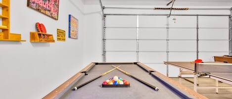 A pool table with balls, a ping pong table, and a wooden shelf with shoes.