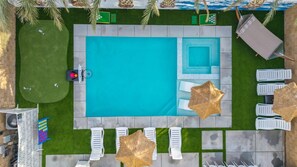 Ein rechteckiger Pool mit umlaufender Liegefläche, Liegestühlen und Sonnenschirmen.