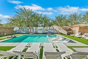 A swimming pool with a basketball hoop, lounge chairs, and palm trees.