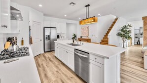 Una cocina moderna con armarios blancos, electrodomésticos de acero inoxidable y una escalera de madera.