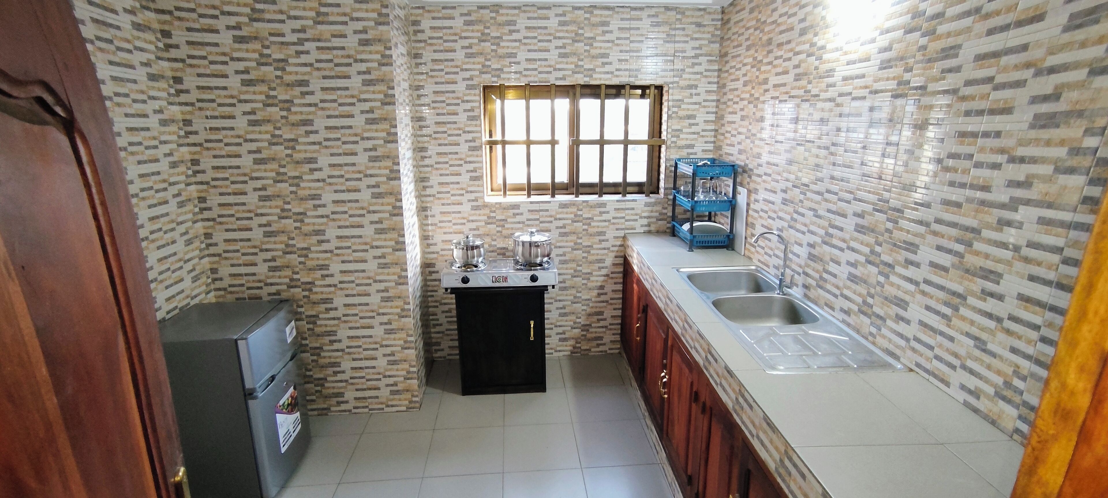 A compact kitchen with a refrigerator, a stove, a sink, and a window with bars.