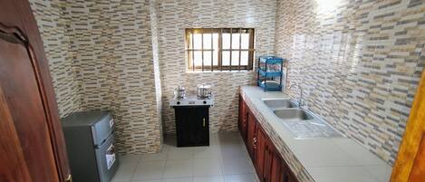 A compact kitchen with a refrigerator, a stove, a sink, and a window with bars.