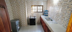 Cocina compacta con refrigerador, estufa, pileta y ventana con rejas.