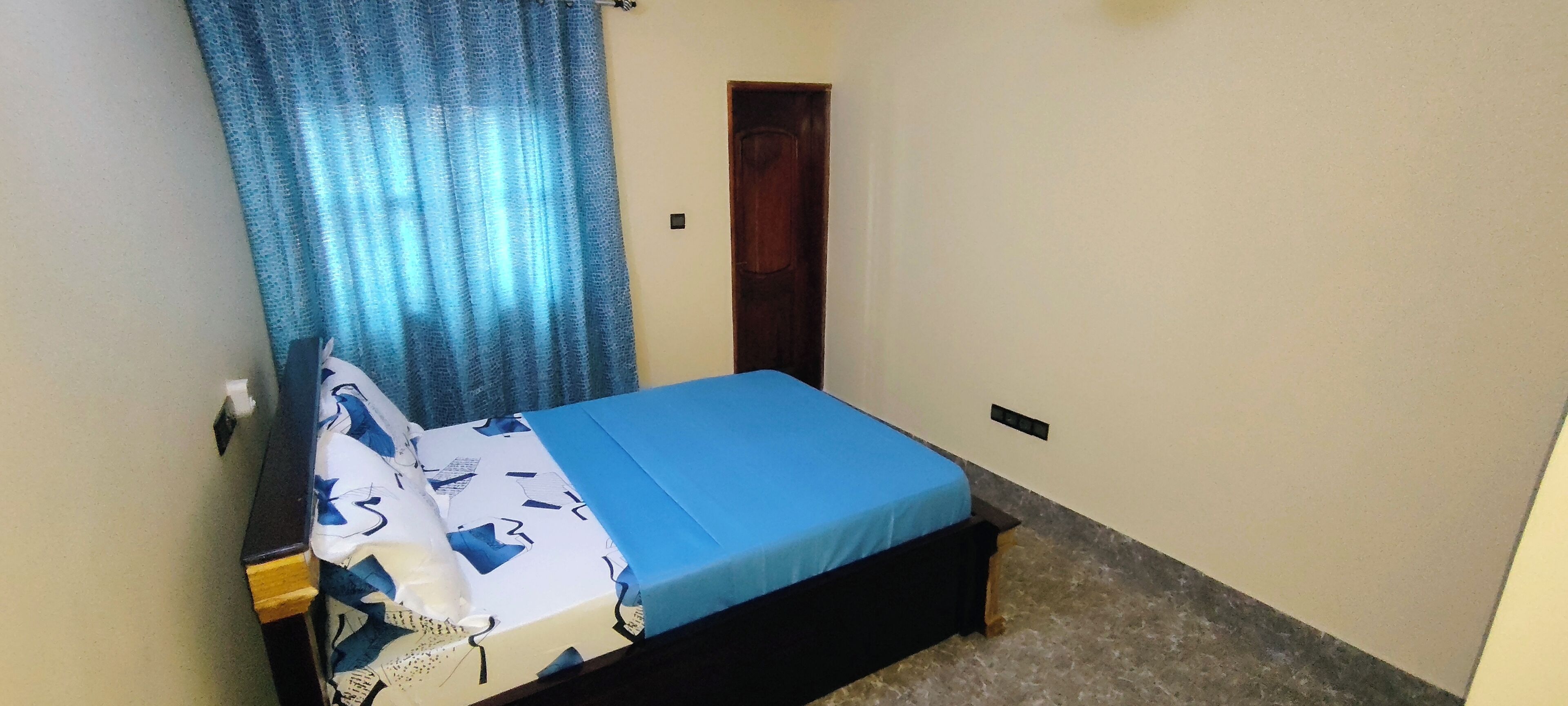 Ein kleines Schlafzimmer mit einem Einzelbett, einem Holz-Kopfteil, einer blauen Bettdecke und einem blauen Vorhang.
