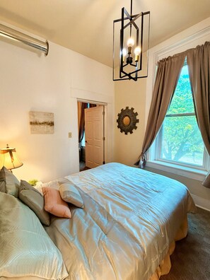 A bedroom with a bed, a hanging light fixture, a door, and a window with curtains.