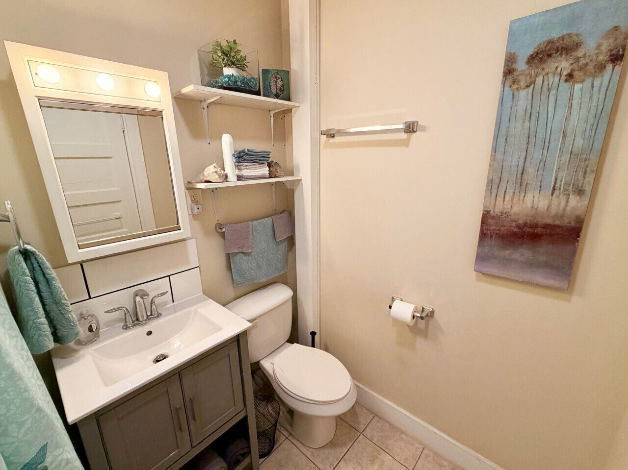 A bathroom with a white sink, mirror, and toilet, with a towel rack and shelves above the sink.