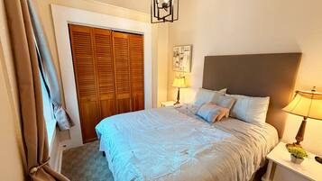 A bedroom with a bed, bedside tables, a lamp, a door, and a wall-mounted artwork.