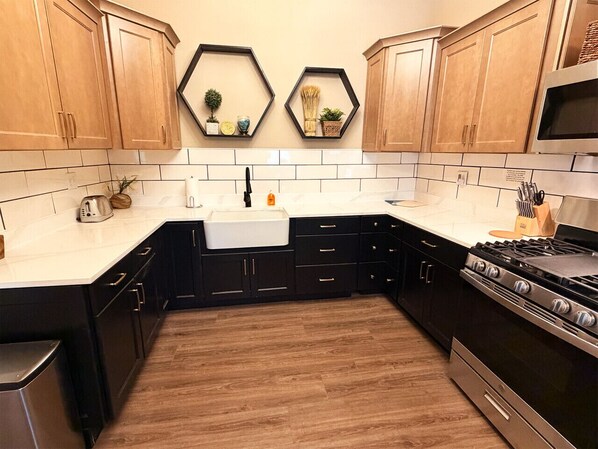 A kitchen with wooden cabinets, a white countertop, a stainless steel stove, and a white sink.