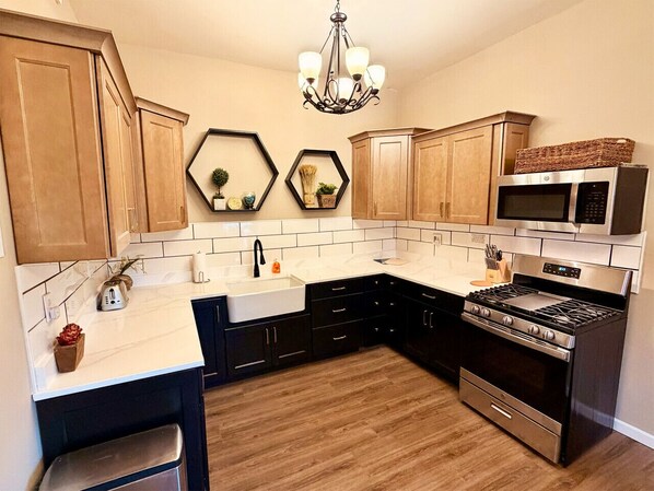 A kitchen with wooden cabinets, a white countertop, a stainless steel stove, a microwave, and a chandelier.