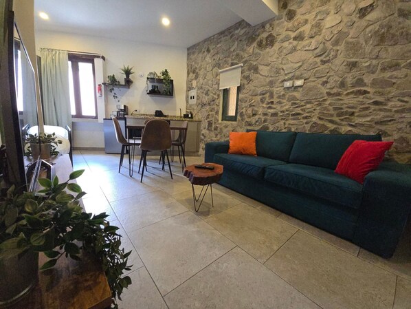 Ein Wohnzimmer mit Steinsandsteinwand, einem blauen Sofa, einem Essbereich mit Stühlen und einer Küche im Hintergrund.