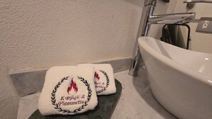 Two white towels with embroidered text and a laurel wreath design on a dark countertop next to a white sink. - Loft Il Rifugio di Fiammetta (Val'Quirico)