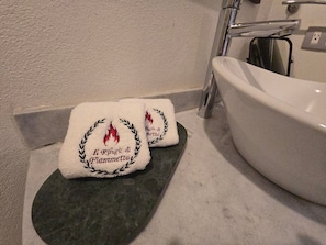 Zwei weiße Handtücher mit eingesticktem Text und einem Lorbeerkranz-Design auf einer dunklen Arbeitsplatte neben einem weißen Waschbecken.