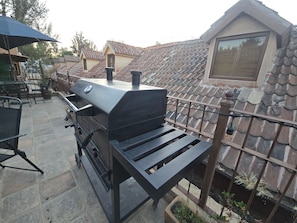 Ein Grill mit Tisch in einem Garten mit Ziegeldächern und einem Haus im Hintergrund.
