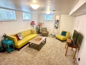 Ein Wohnzimmer mit gelbem Sofa, Couchtisch, TV-Möbel und einem kleinen Tisch mit Pflanze.