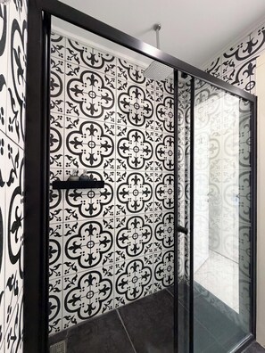 A modern bathroom with patterned tiles, a glass shower enclosure, and a black towel rack. - ASİA HOTEL (Bodrum)