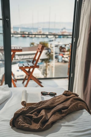 A bed with a book and sunglasses, a brown blanket, and a view of a marina through a window. - ASİA HOTEL (Bodrum)