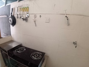Une cuisine équipée d’une cuisinière, d’un étendoir suspendu pour les ustensiles et d’une prise électrique fixée au mur.