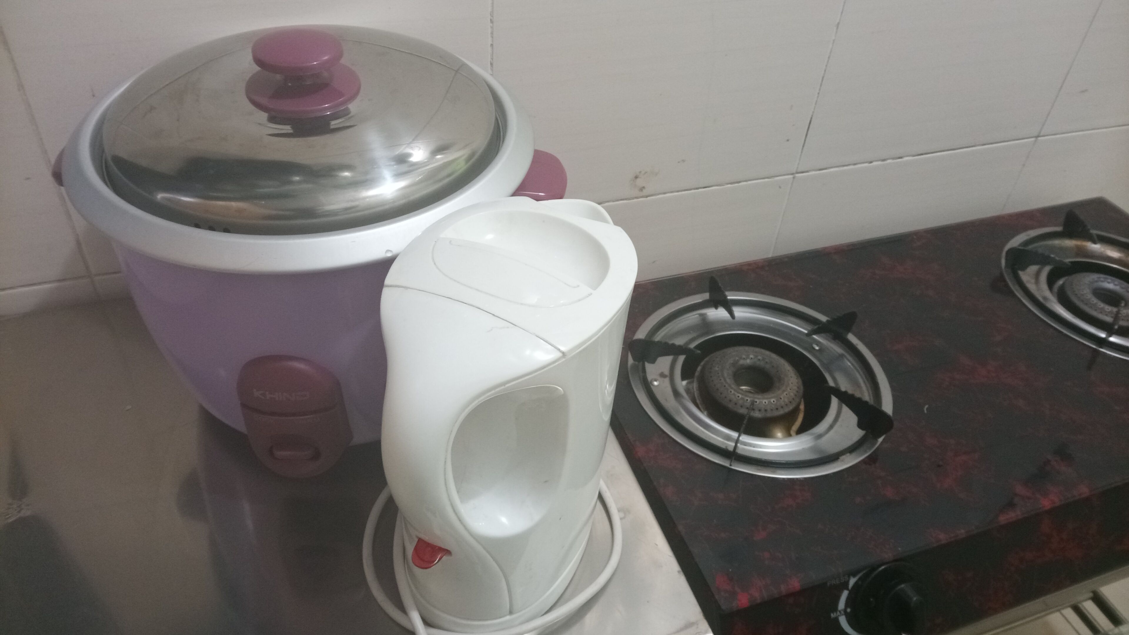 A kitchen with a pink slow cooker, a white electric kettle, and a gas stove.