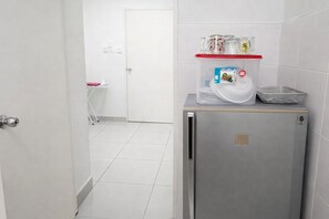 Une cuisine compacte équipée d’un réfrigérateur, d’un four à micro-ondes et d’une petite étagère contenant des ustensiles de cuisine.