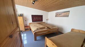 A room with a wooden ceiling, a bed with a beige blanket, a small table with a lamp, and a wall-mounted picture. - Vacation apartment with green garden view (Ahrenshoop)
