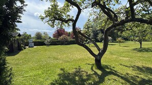 A grassy outdoor area with trees and a building in the background. - Vacation apartment with green garden view (Ahrenshoop)